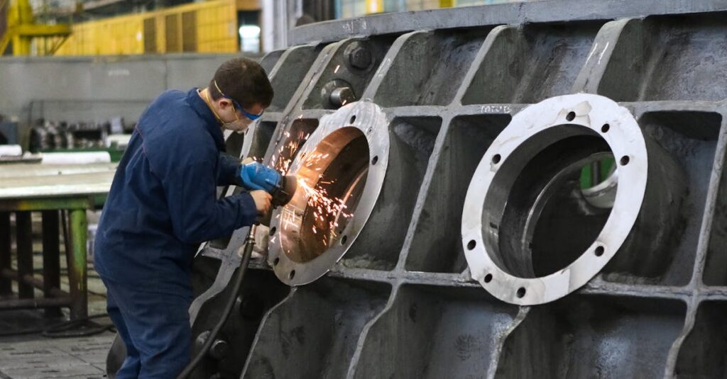 A worker in protective gear grinding metal, creating sparks in a factory setting.