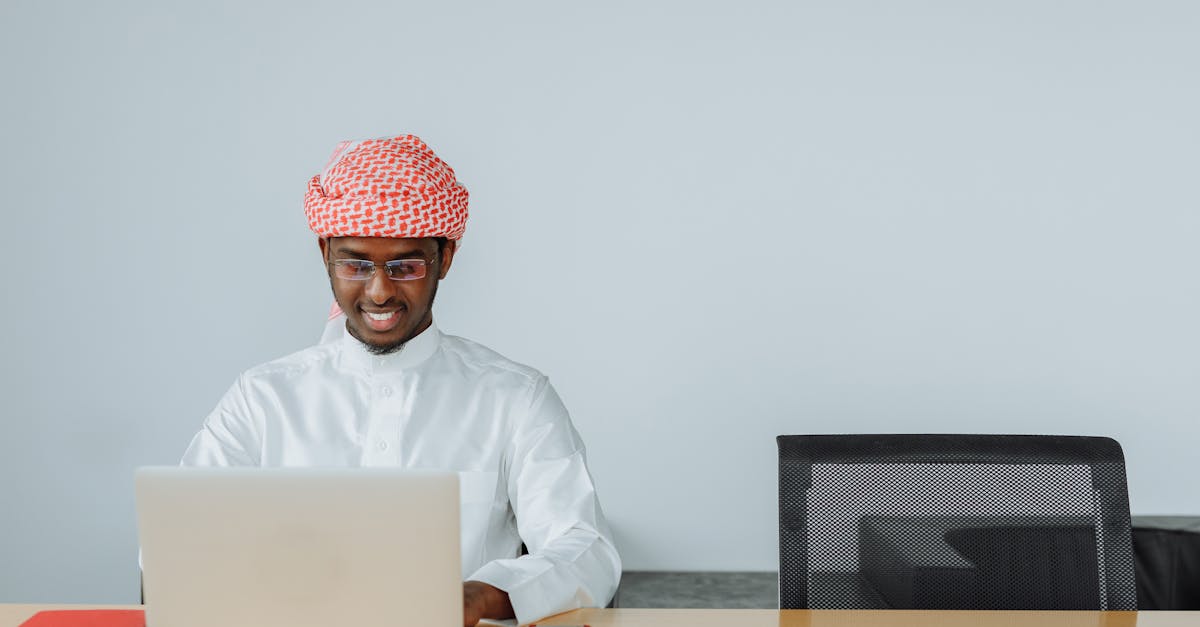 Middle Eastern man in traditional attire using a laptop at his office desk, smiling while working.